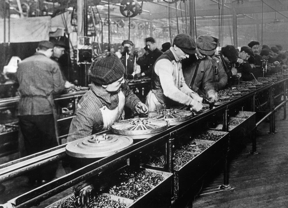 Linha de montagem da Ford em 1913: operários trabalham ao longo de uma esteira, sem eixos nem correias no teto.